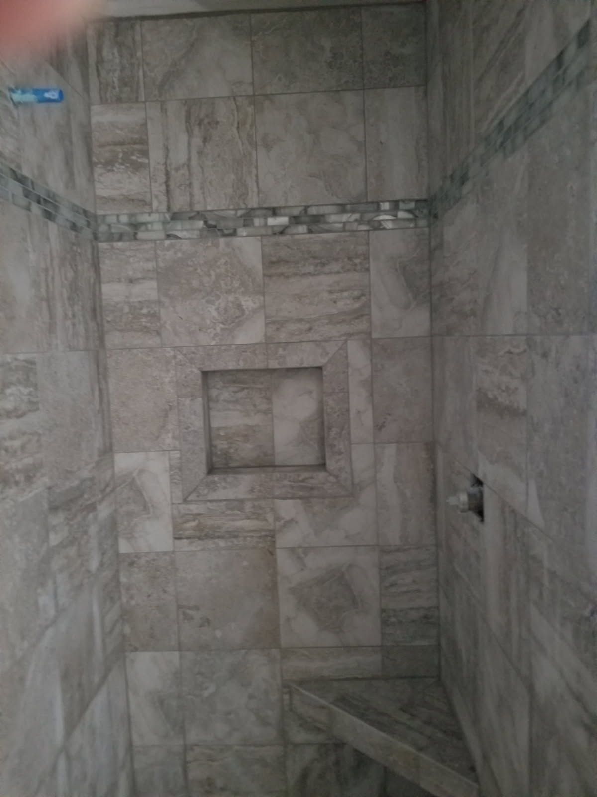 A tiled shower with a shelf in the wall and a bench.