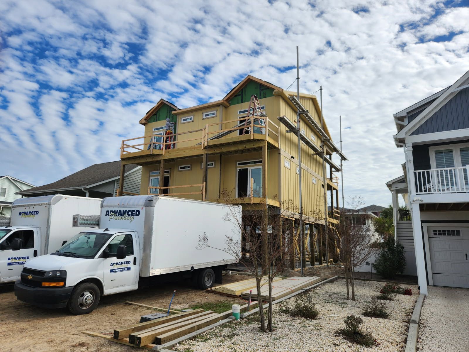 Two white trucks are parked in front of a house under construction.