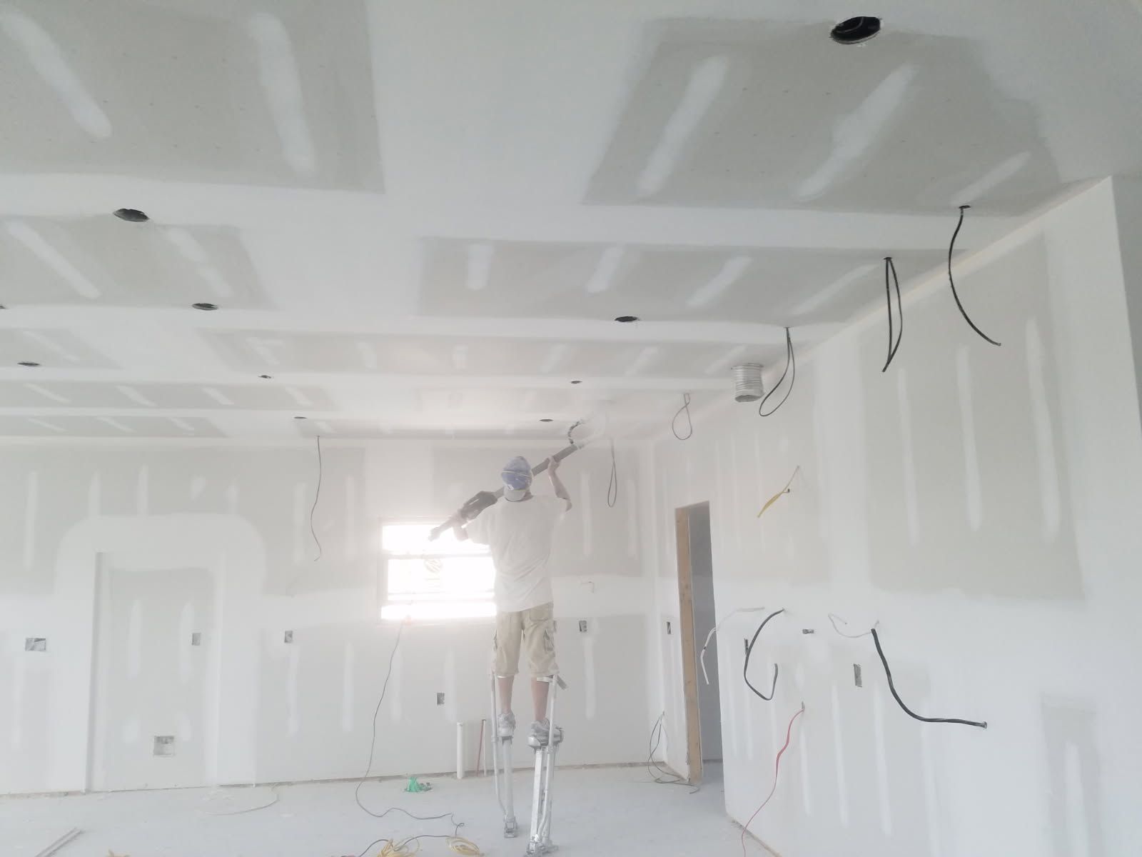 A man is standing on a ladder painting the ceiling of a room.