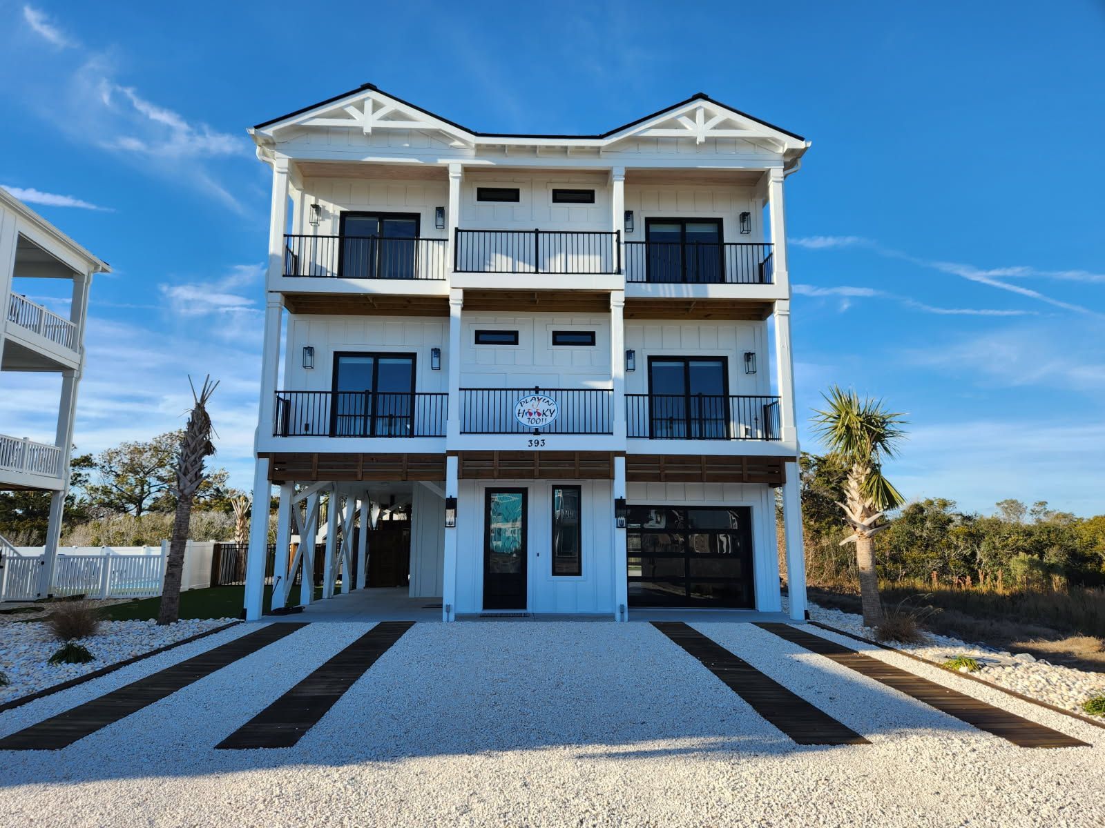 A large white house is sitting on top of a gravel driveway.