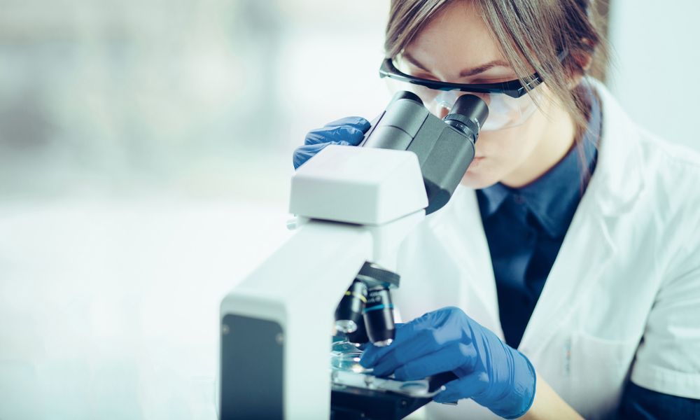 A Woman is Looking Through a Microscope in a Laboratory — Northern Beaches GP Superclinic in Deeragun, QLD