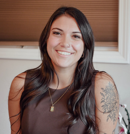 A woman in a plaid sweater is standing in front of a brick wall.