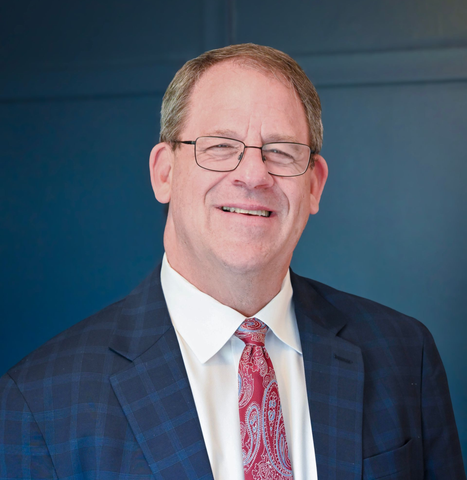 A man in a suit and tie is pointing at the camera