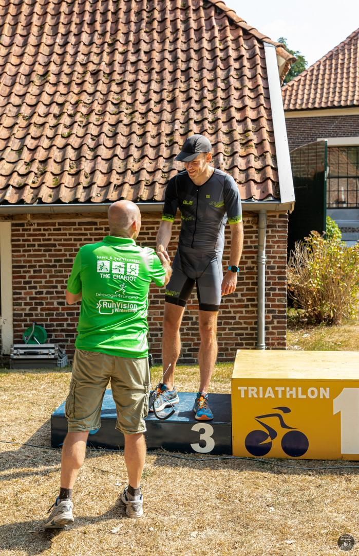 Een man in een groen shirt schudt de hand van een man die op een podium staat.