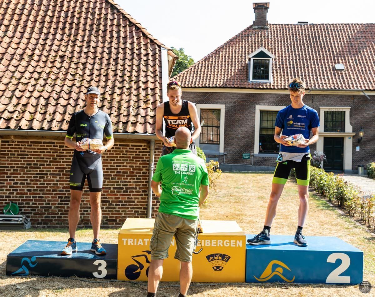 Drie mannen staan ​​op een podium voor een bakstenen gebouw.