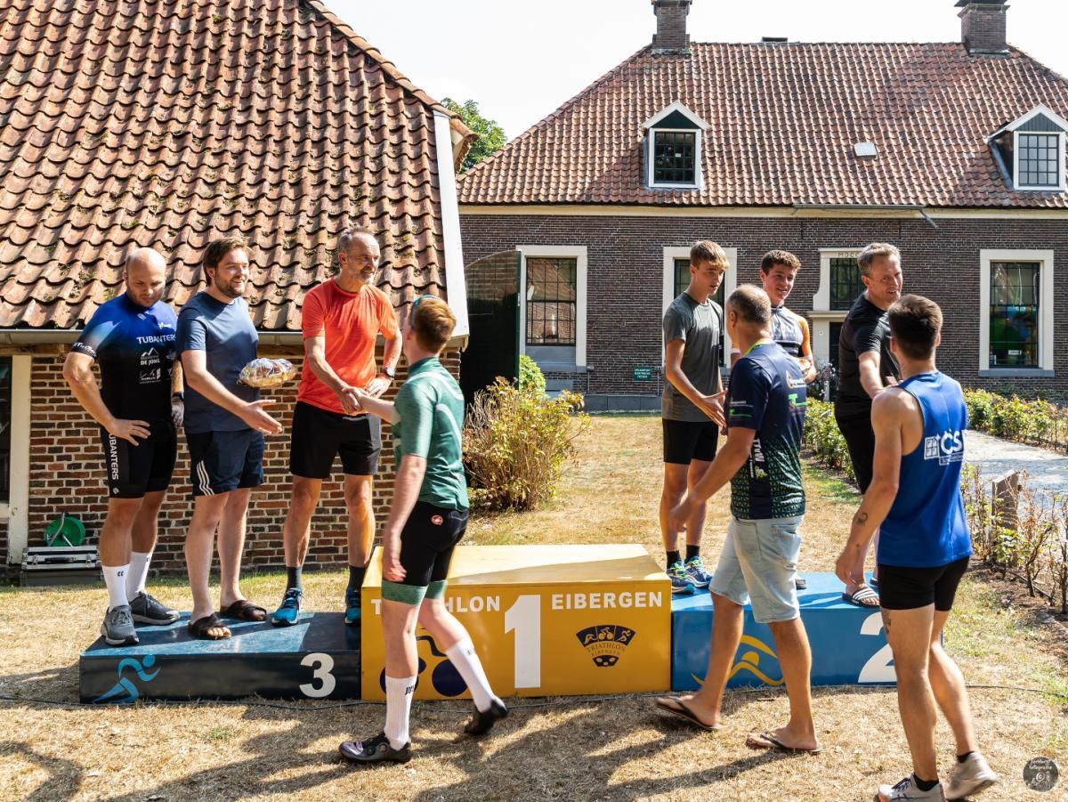 Een groep mensen staat op een podium voor een bakstenen gebouw.