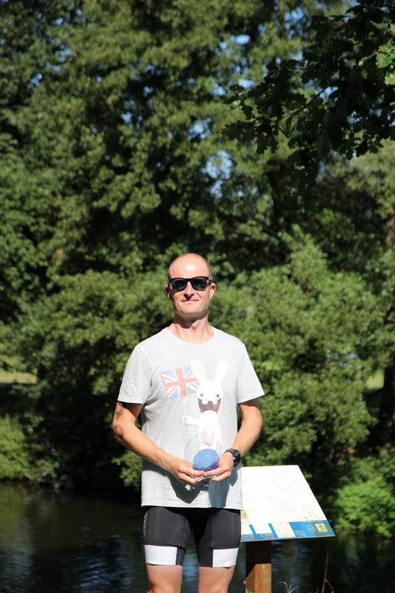 Een man in een grijs shirt en een zwarte korte broek staat voor een rivier.