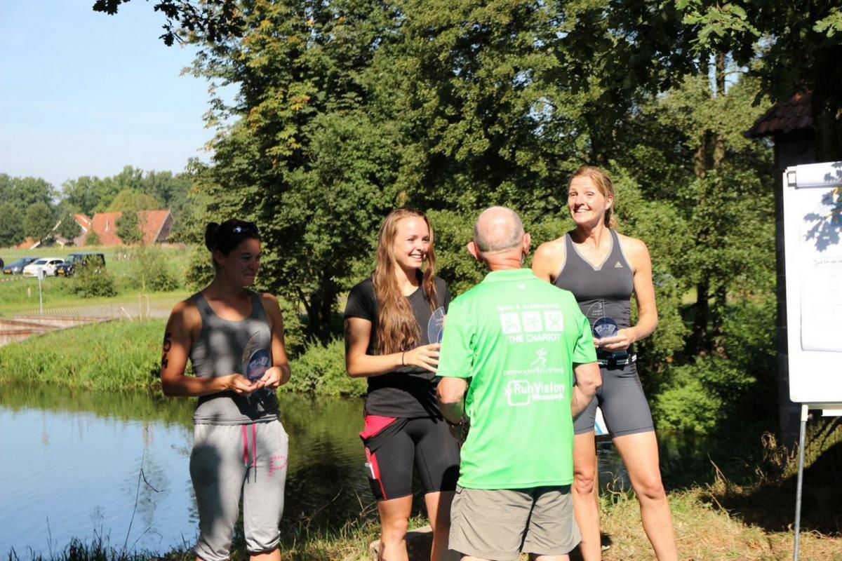 Een man in een groen shirt praat met drie vrouwen aan de rand van een meer.