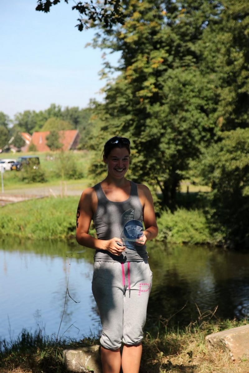 Een vrouw staat naast een watermassa en houdt een trofee vast.