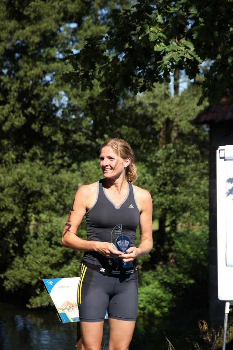 Een vrouw staat voor een rivier en houdt een trofee vast.