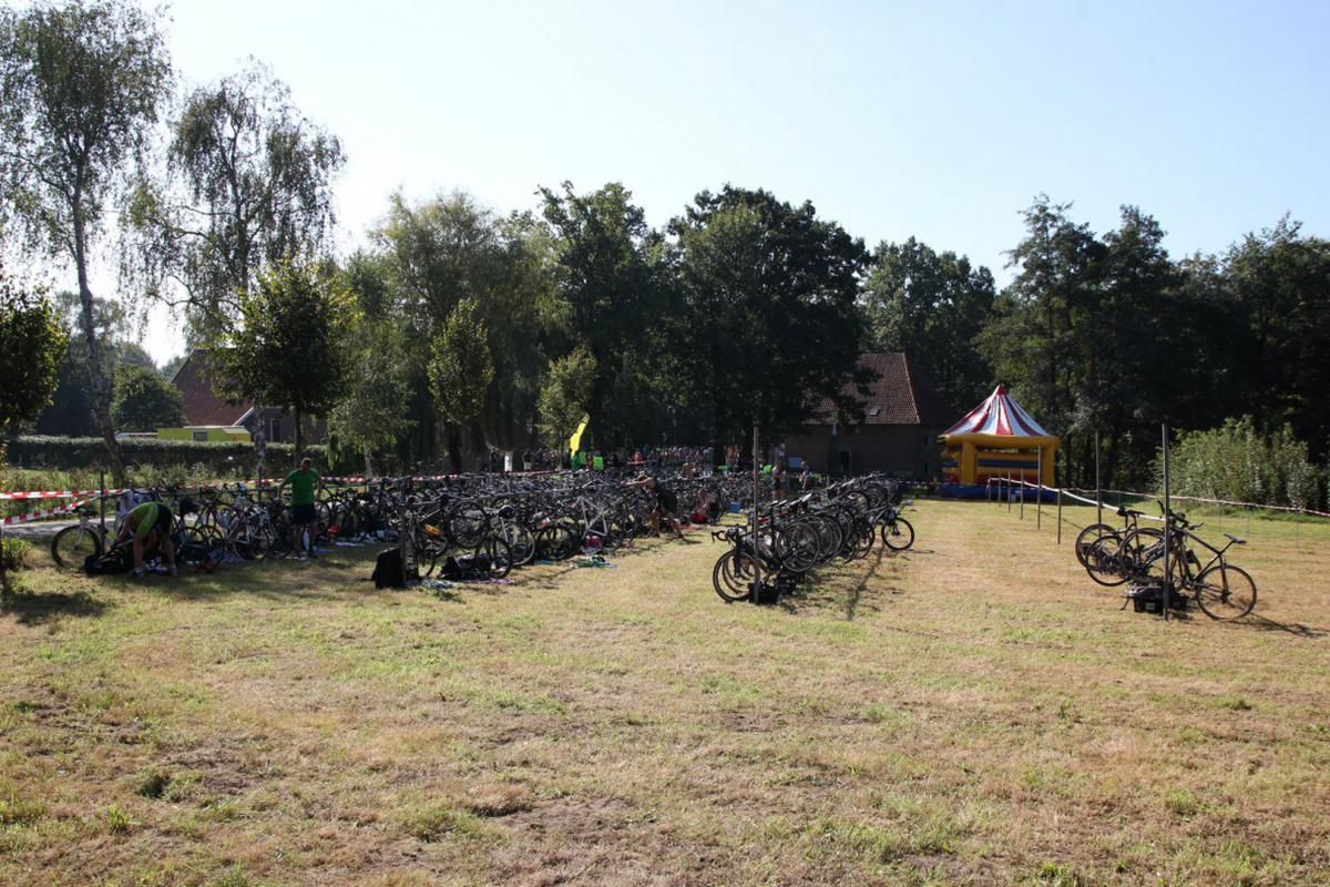 Een aantal fietsen staat geparkeerd in een veld met bomen op de achtergrond.