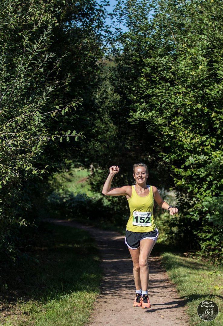 Een vrouw rent over een zandpad in het bos.