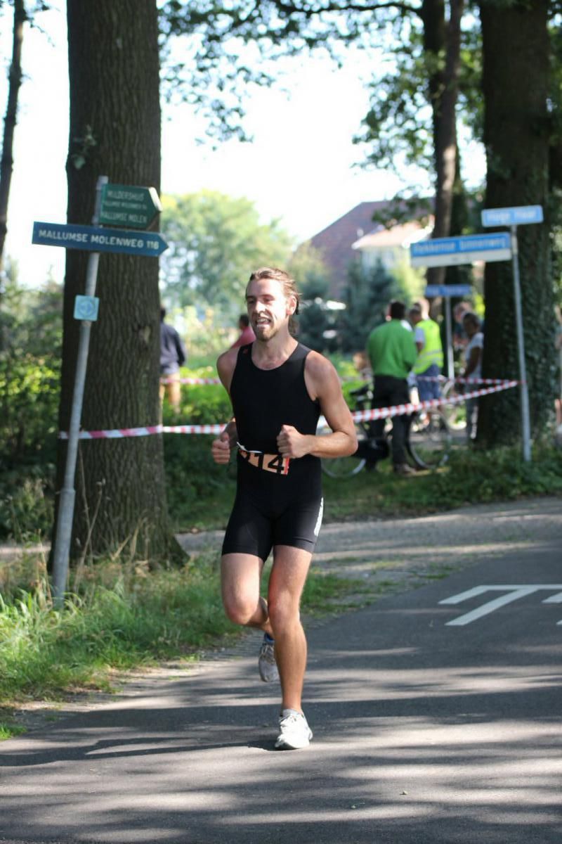 Een man in een zwart tanktopje en korte broek rent op een weg