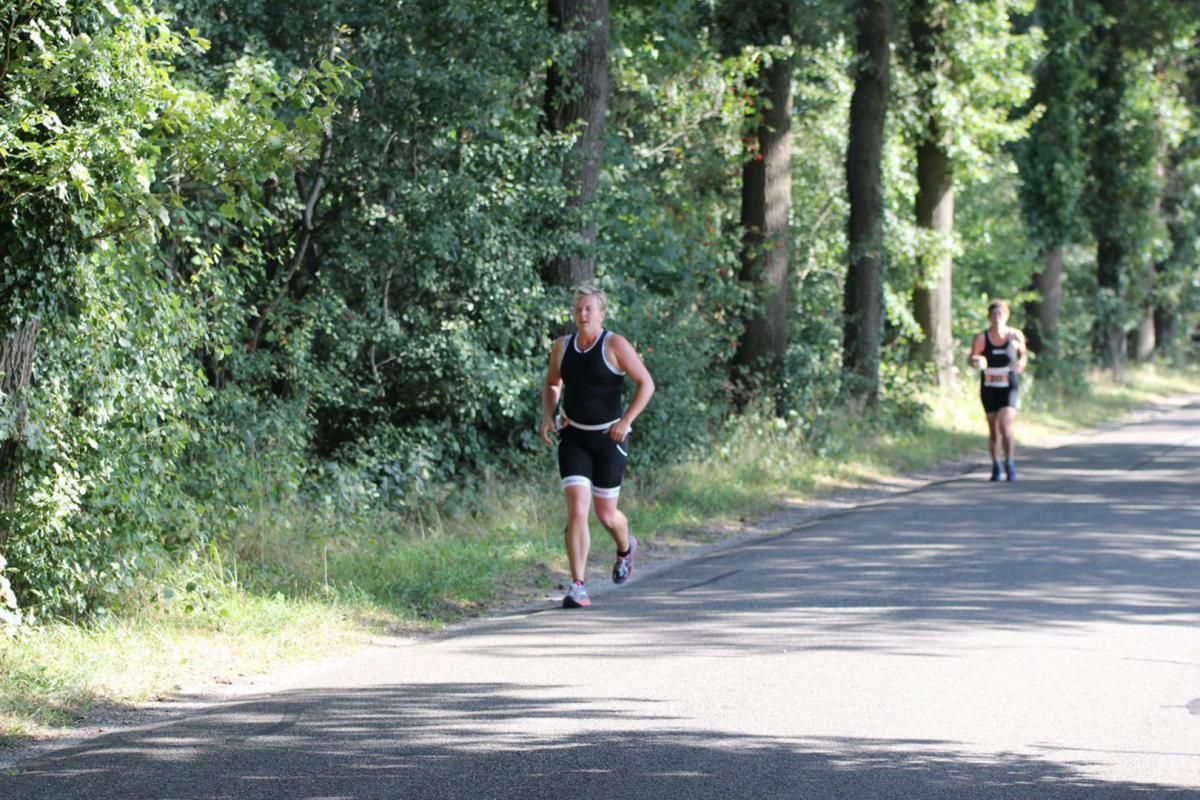 Twee mensen rennen over een weg in het bos.