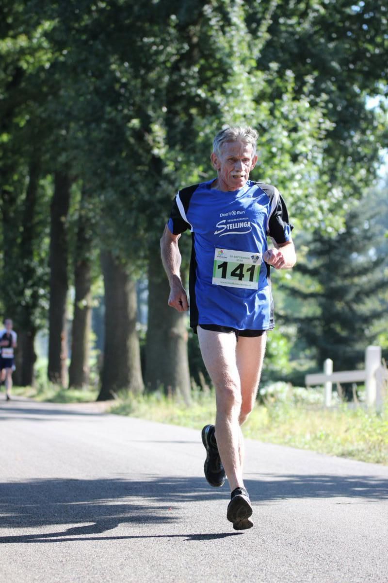 Een man in een blauw shirt en korte broek rent over de weg.