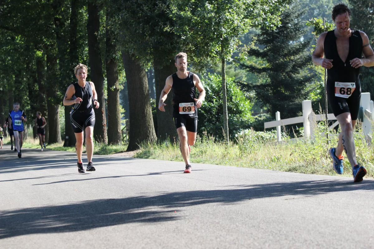 Een groep mensen rent over een weg en een van hen heeft het nummer 66 op zijn shirt