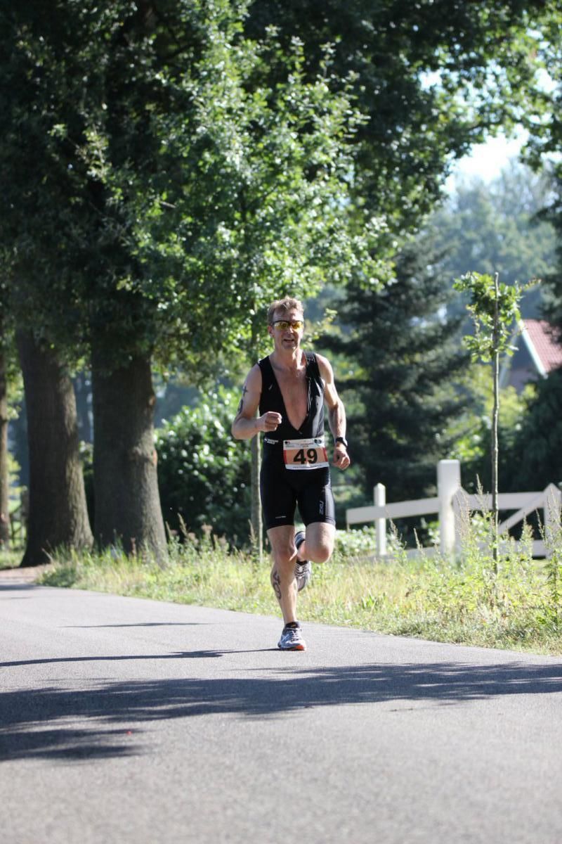 Een man rent over een weg met bomen op de achtergrond.