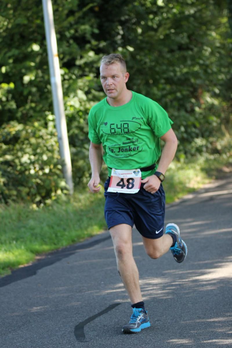 Een man in een groen shirt en een blauwe korte broek rent over de weg.