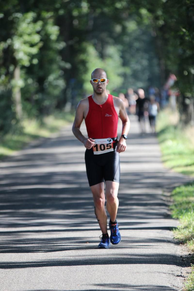 Een man in een rood tanktopje en een zwarte korte broek rent over een pad.