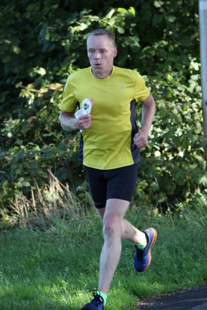 Een man in een geel shirt en een zwarte korte broek rent.