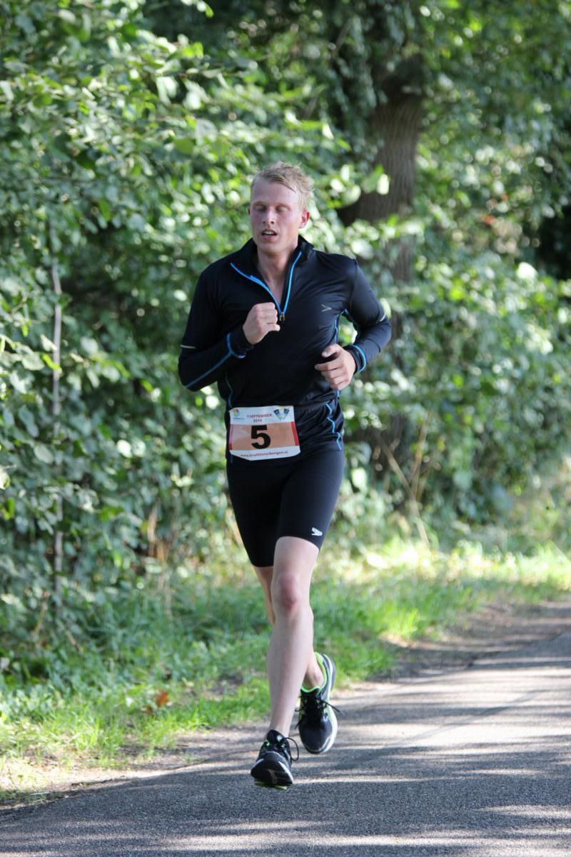 Een man rent op een pad in het bos.
