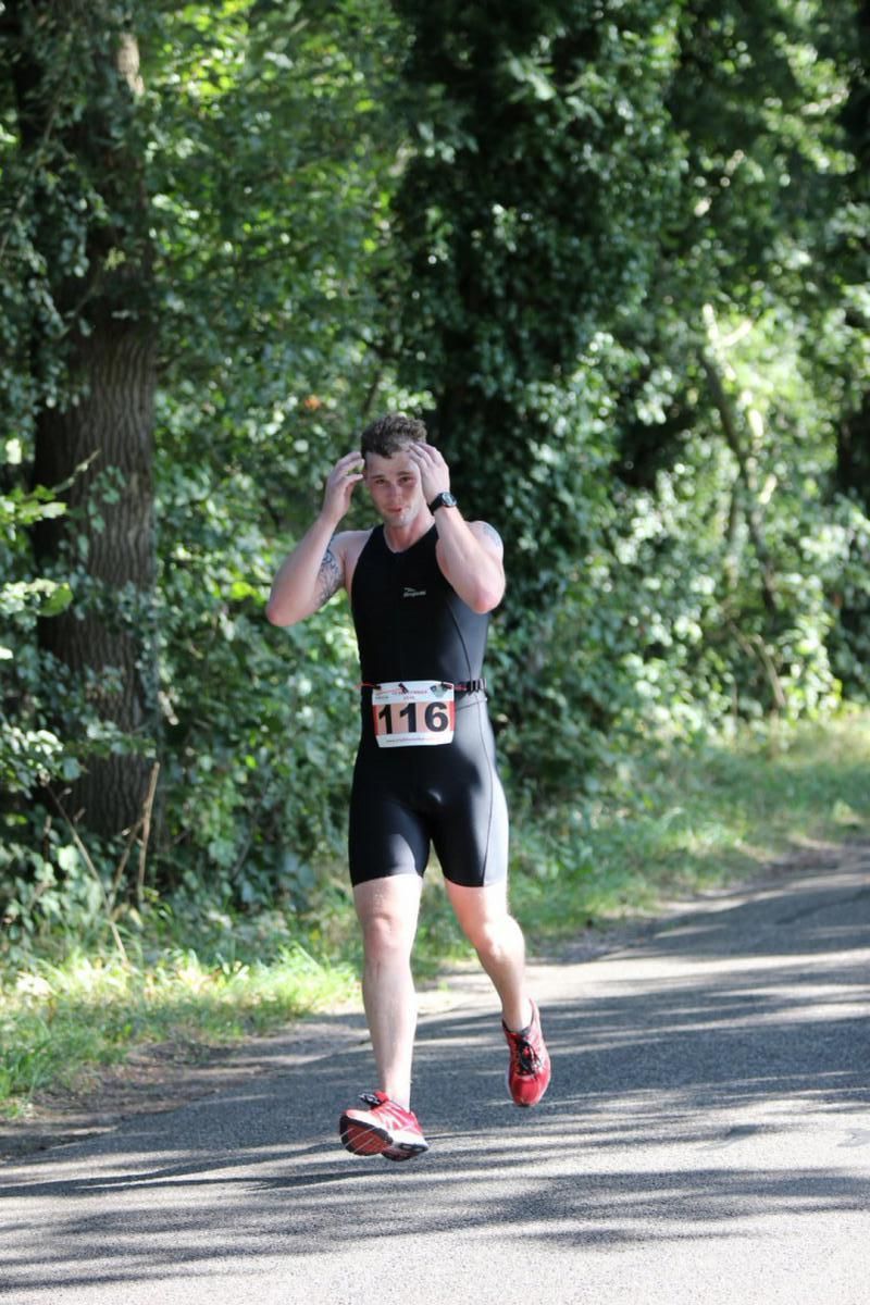 Een man rent over een weg met bomen op de achtergrond.