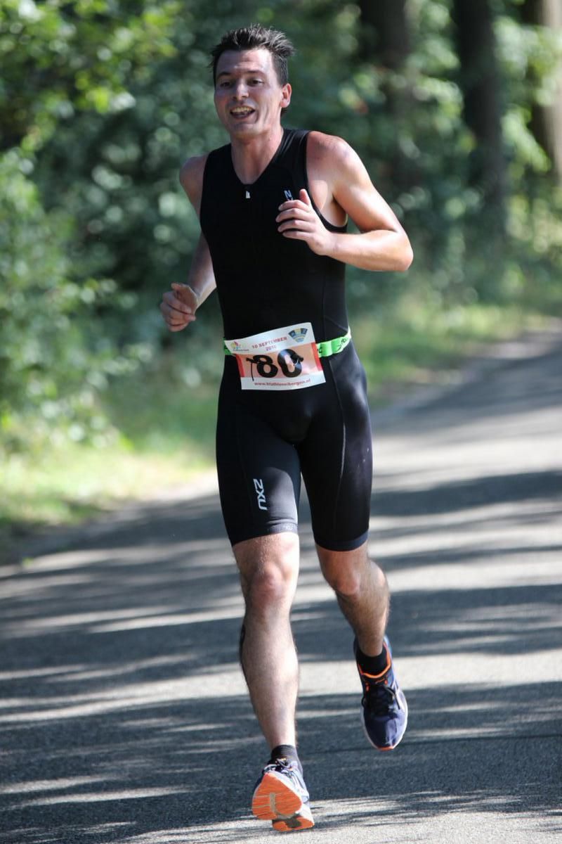 Een man in een zwart tanktopje en korte broek rent over de weg.