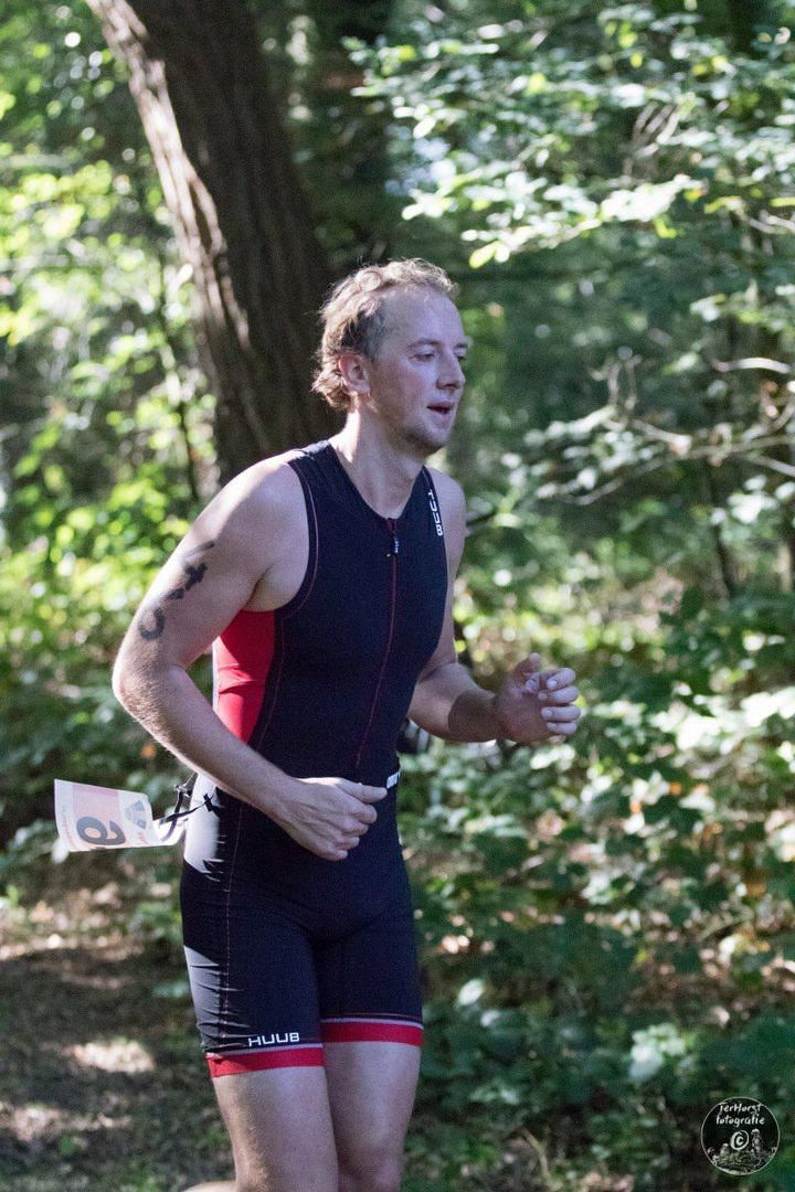 Een man in een zwart en rood tanktop rent door het bos.