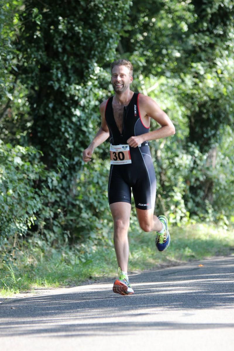 Een man in een triatlonpak rent over de weg.