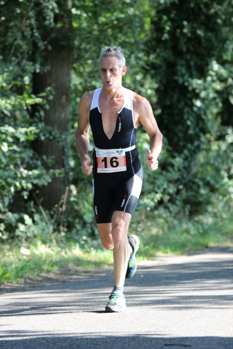 Een man in een triatlonpak rent over de weg.