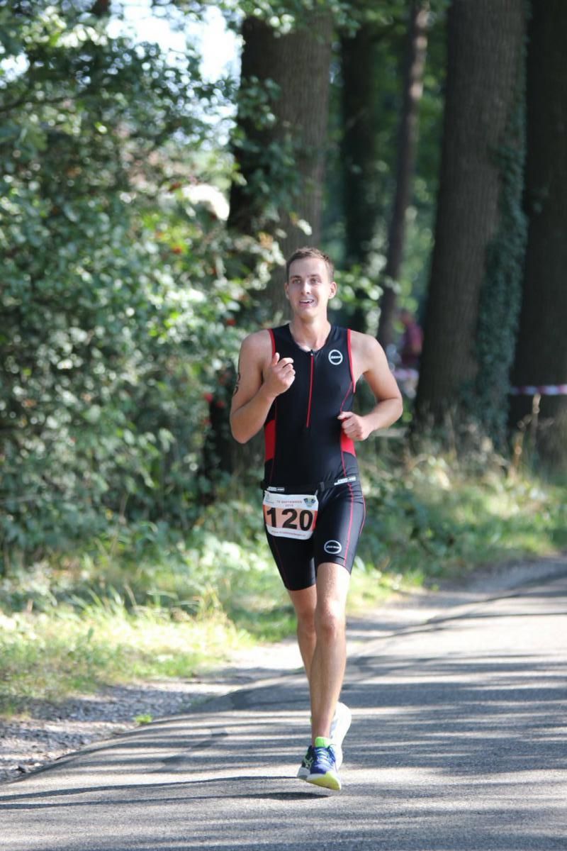 Een man rent over een weg met bomen op de achtergrond.