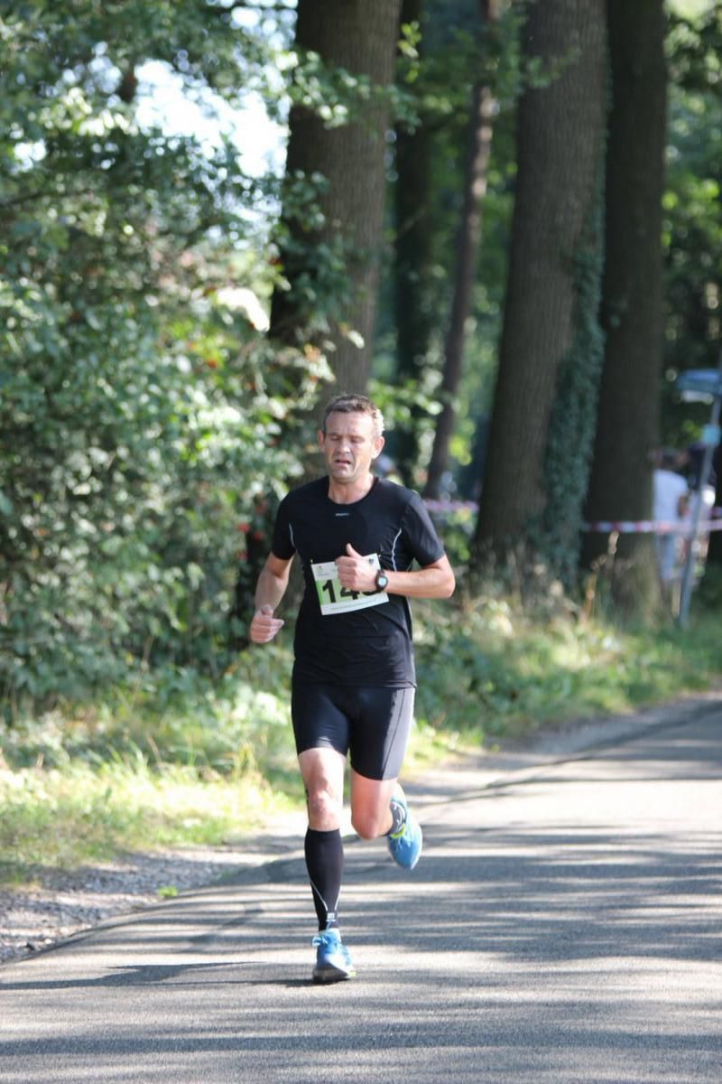 Een man rent over een weg in het bos.