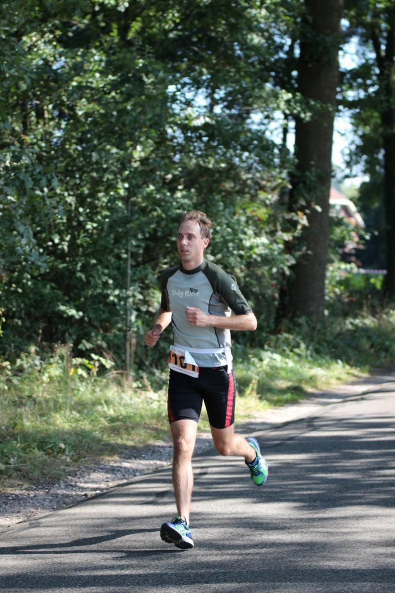 Een man rent over een weg met bomen op de achtergrond