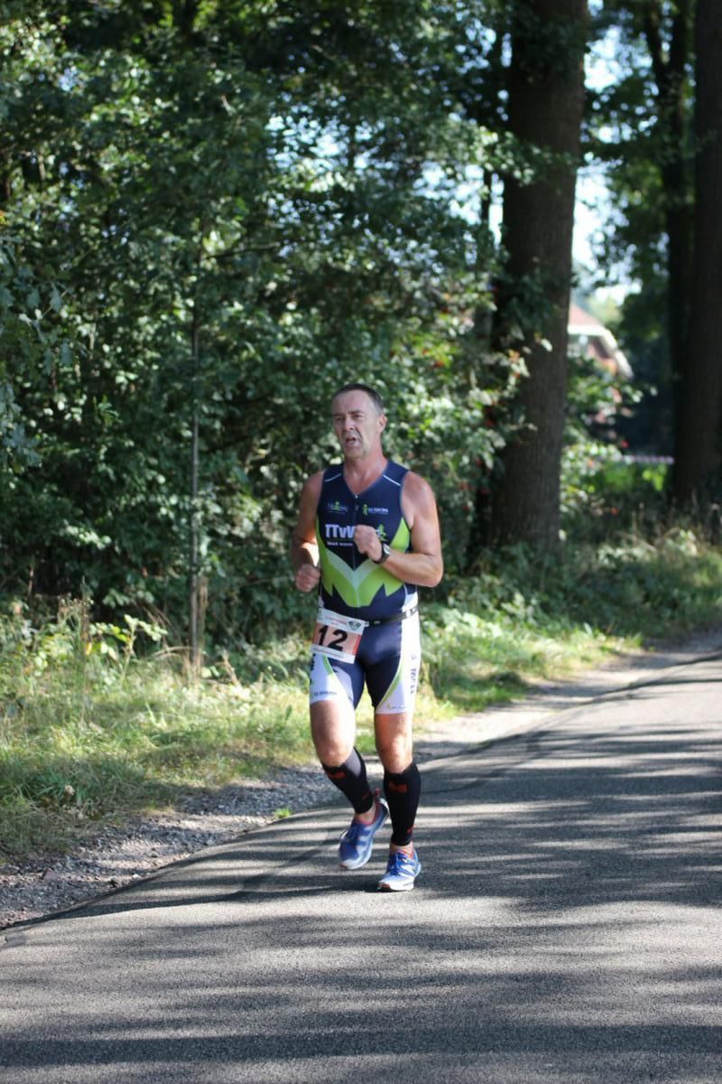 Een man rent over een weg met bomen op de achtergrond.