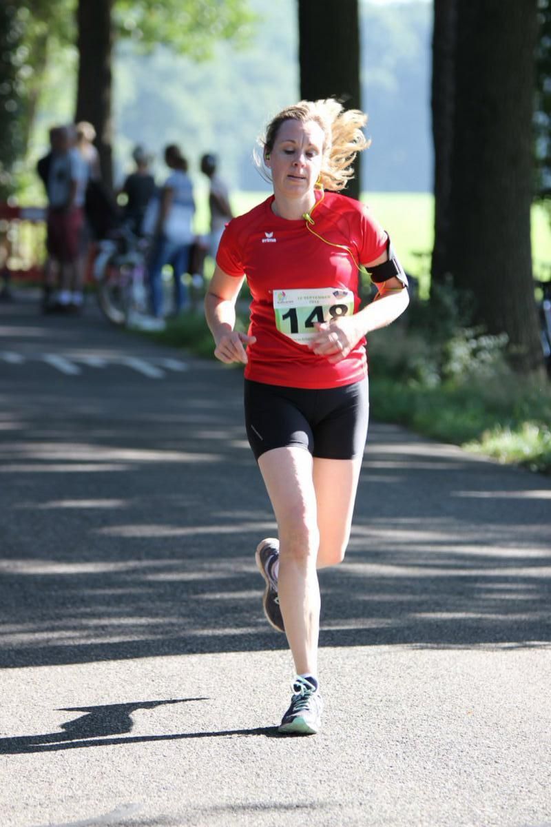 Een vrouw die een rood shirt draagt ​​met het nummer 14 erop rent over een weg