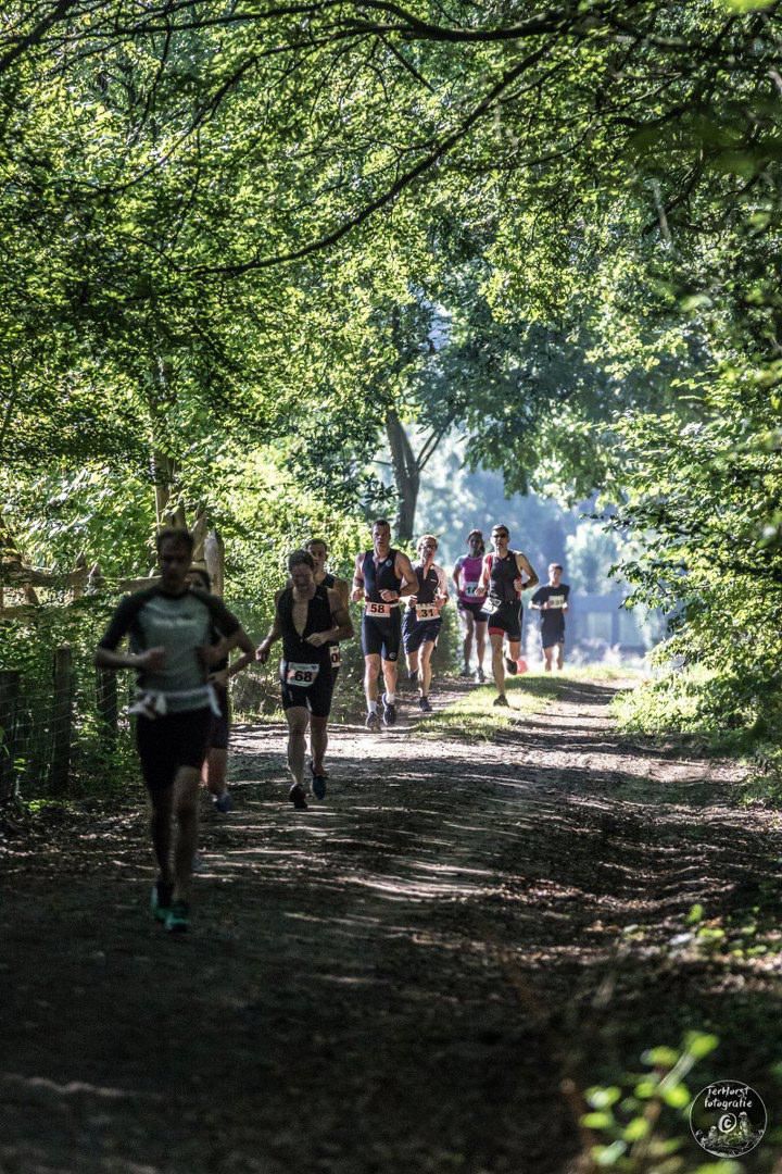 Een groep mensen rent over een zandpad in het bos.