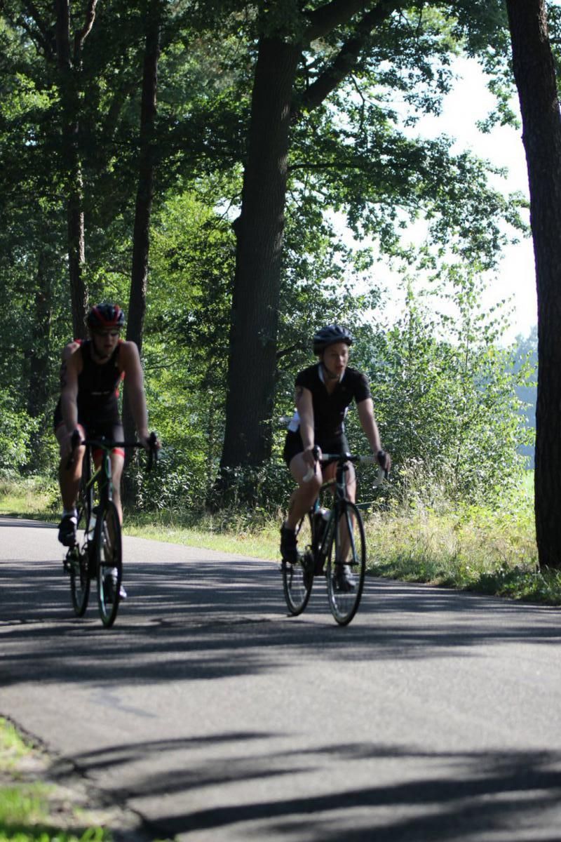 Twee mensen fietsen over een weg die omgeven is door bomen