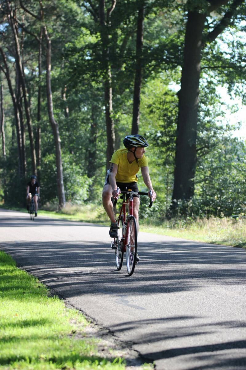 Een man in een geel shirt fietst over een weg