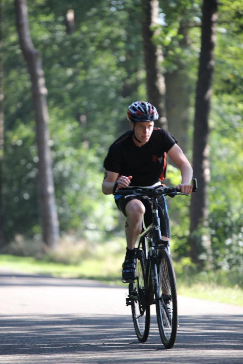 Een man met een helm rijdt op een fiets over de weg.