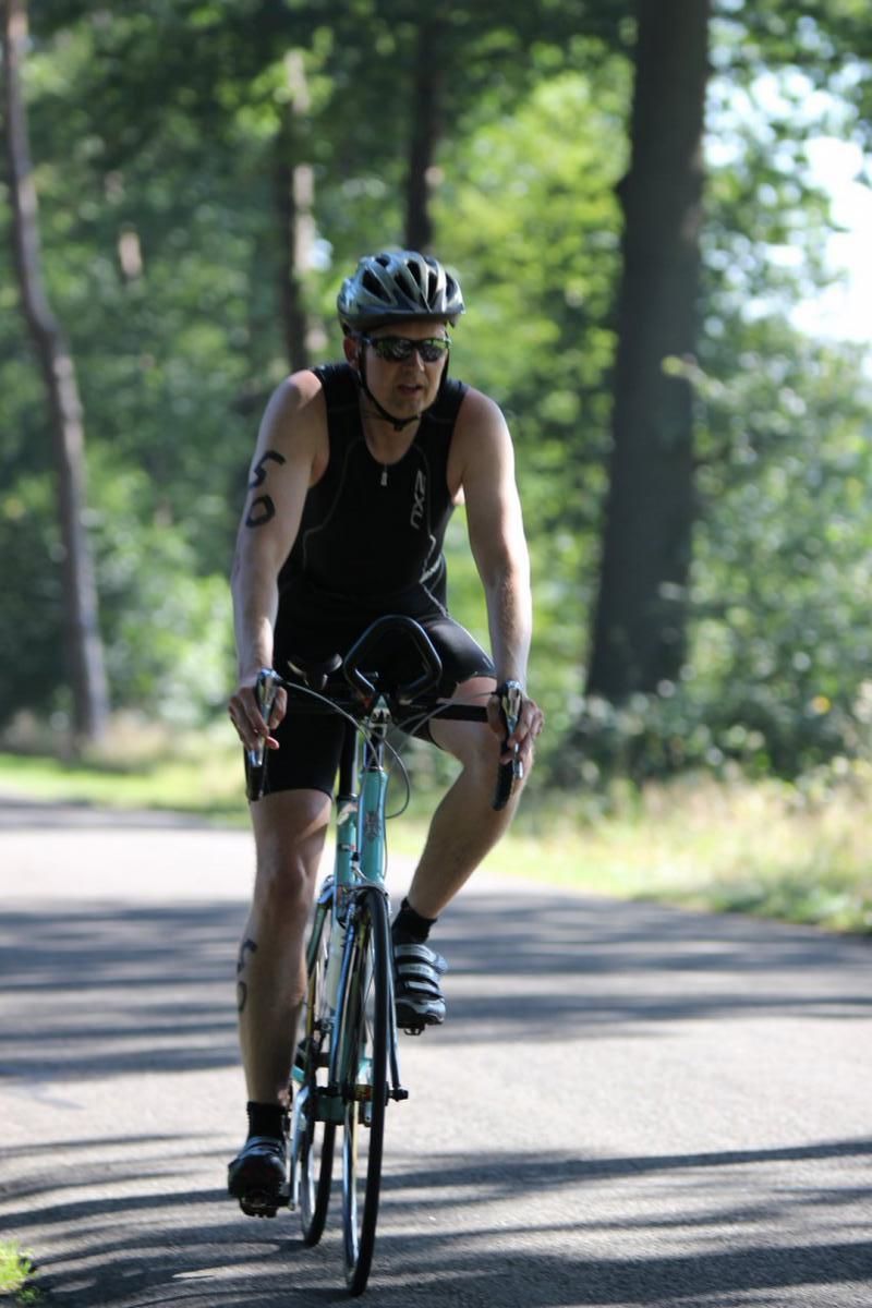 Een man met een helm rijdt op een fiets over de weg.