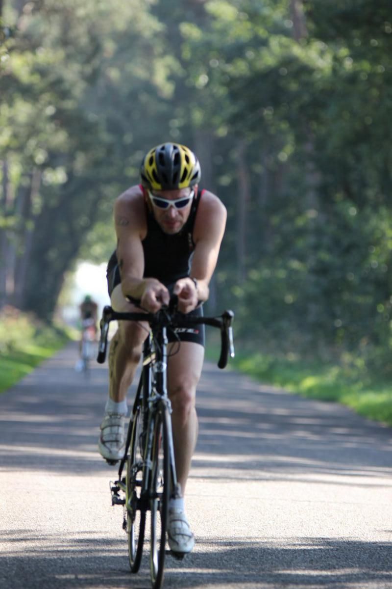 Een man met een helm en een zonnebril rijdt op een fiets over een weg
