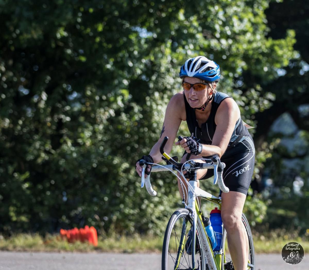 Een vrouw met een helm en een zonnebril fietst over de weg.