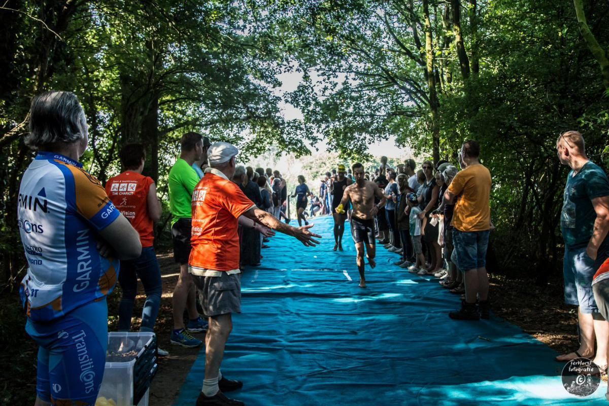 Een groep mensen staat op een blauw zeil en kijkt naar een triatlon.