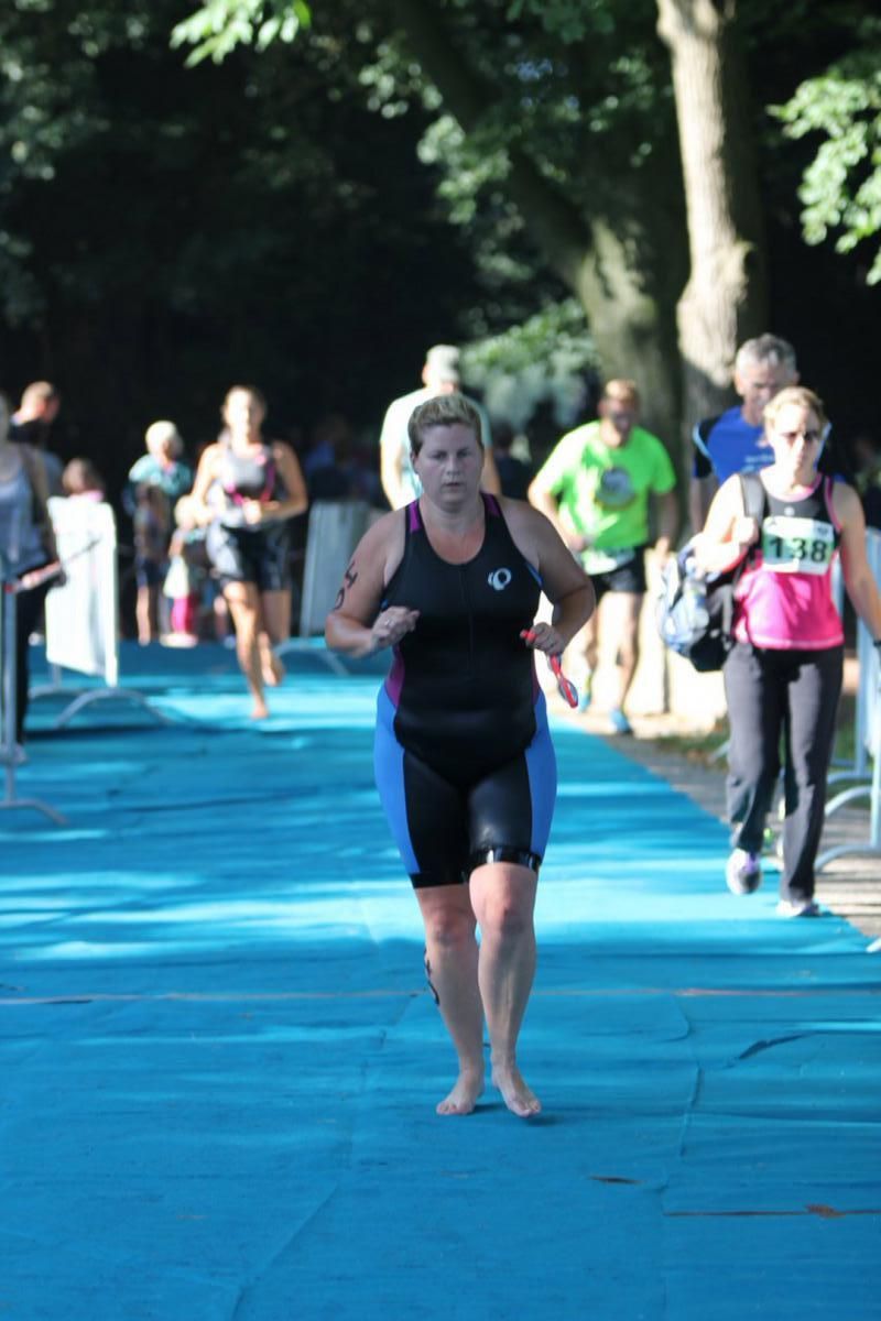 Een vrouw in een zwart tanktopje rent op een blauwe baan