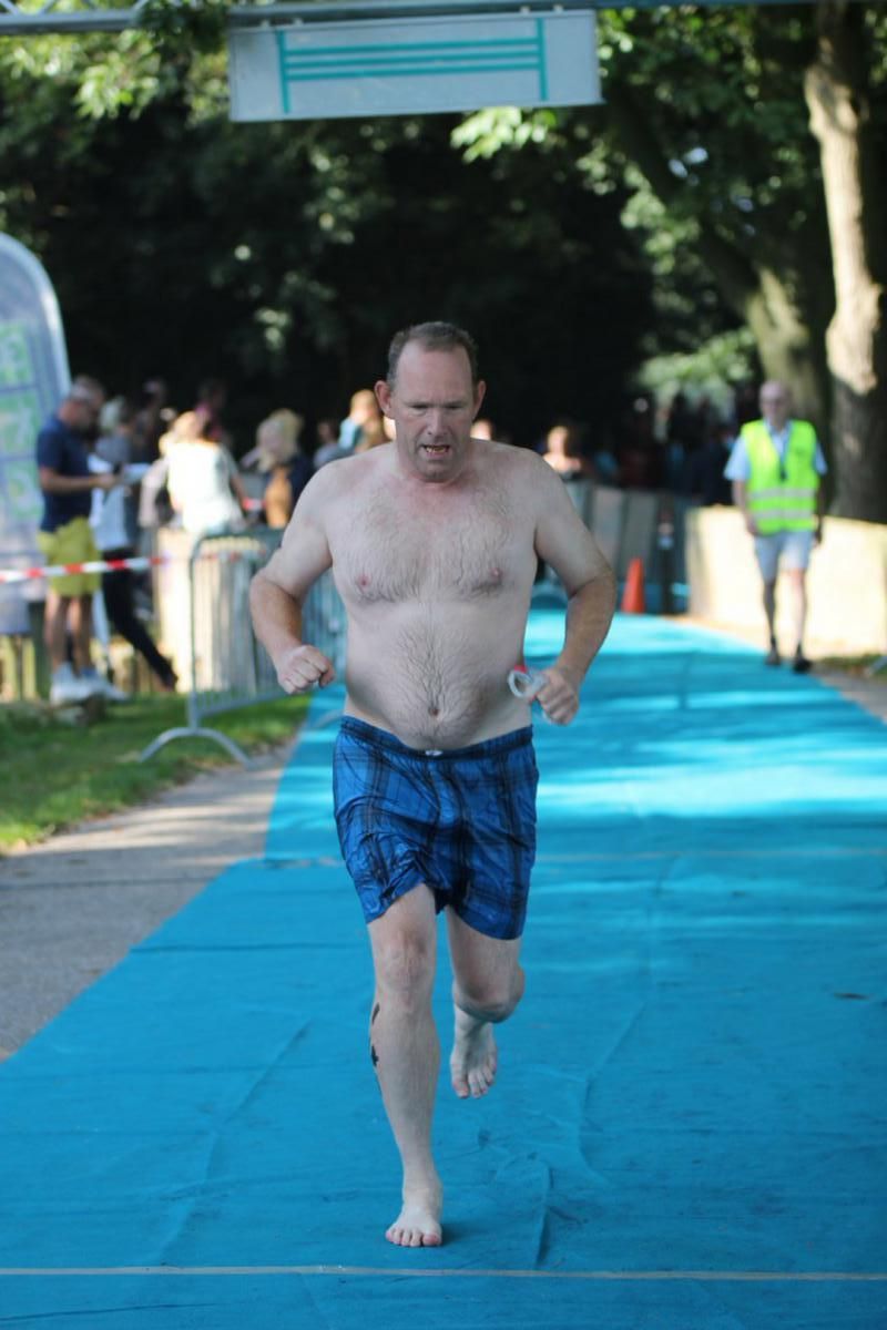 Een man zonder shirt in een blauwe korte broek rent over een blauwe loper.