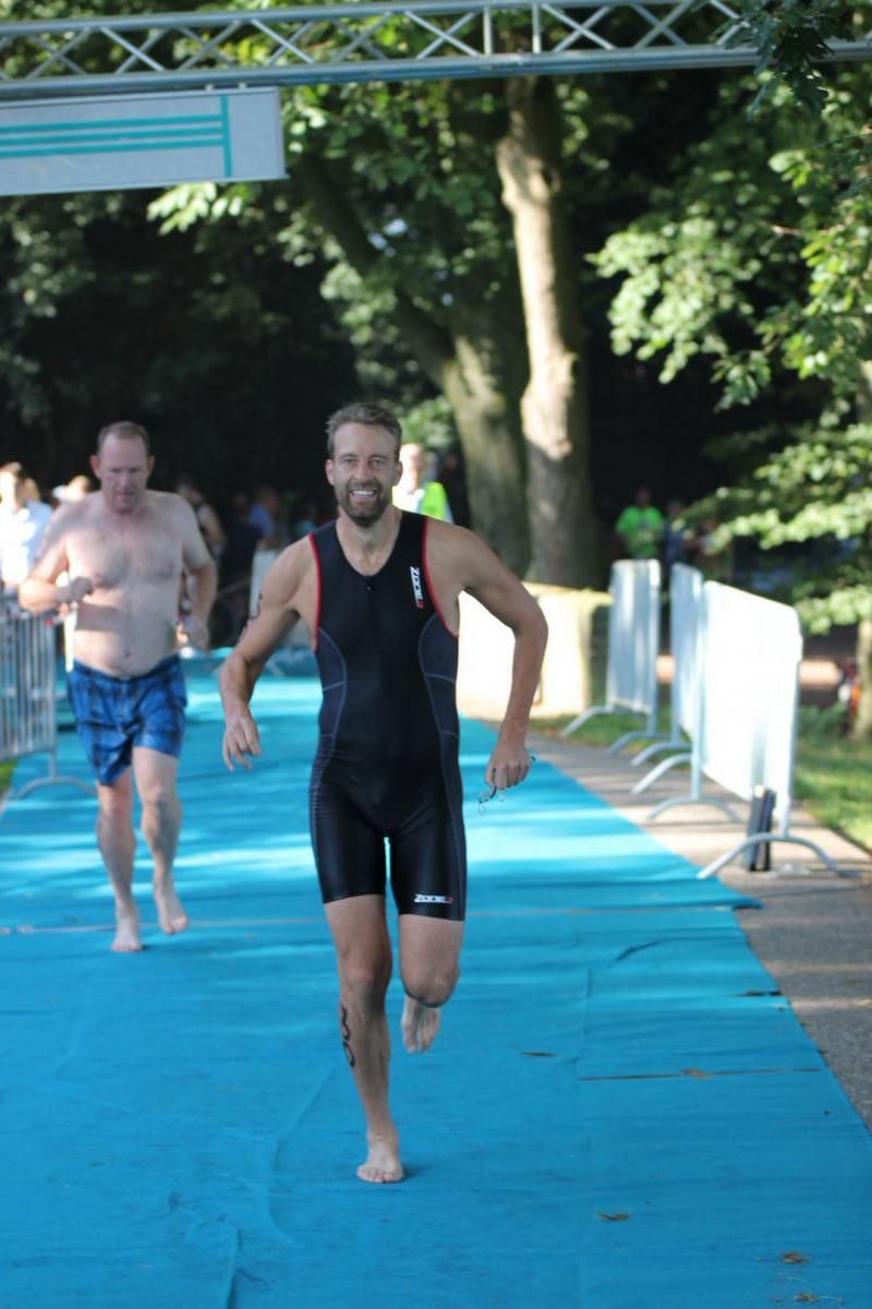 Een man in een wetsuit rent op een blauwe mat.