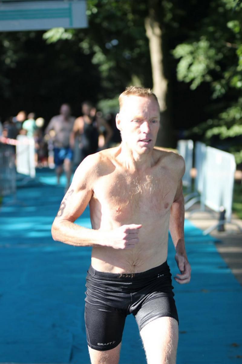 Een man zonder shirt in een zwarte korte broek rent op een blauwe baan