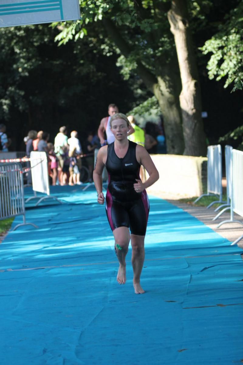 Een vrouw in een wetsuit rent op een blauwe loper.