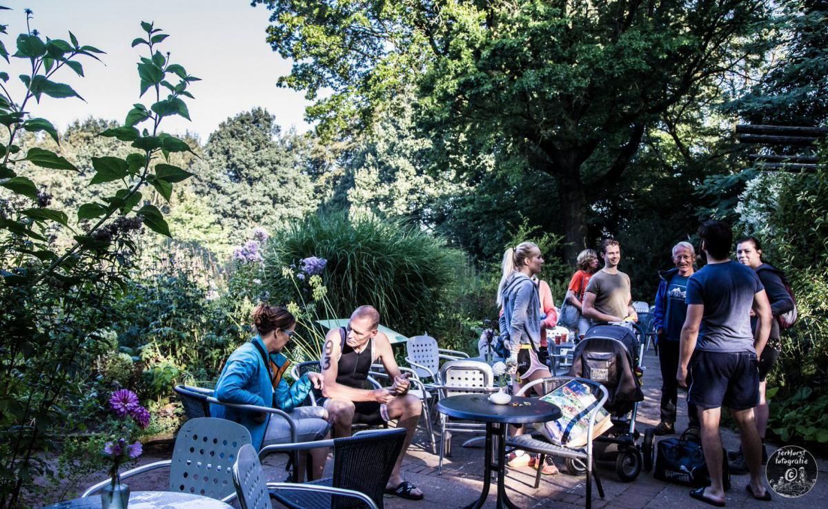 Een groep mensen zit aan tafels in een park.