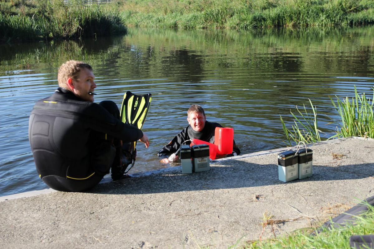 Twee mannen zitten op een steiger naast een watermassa.